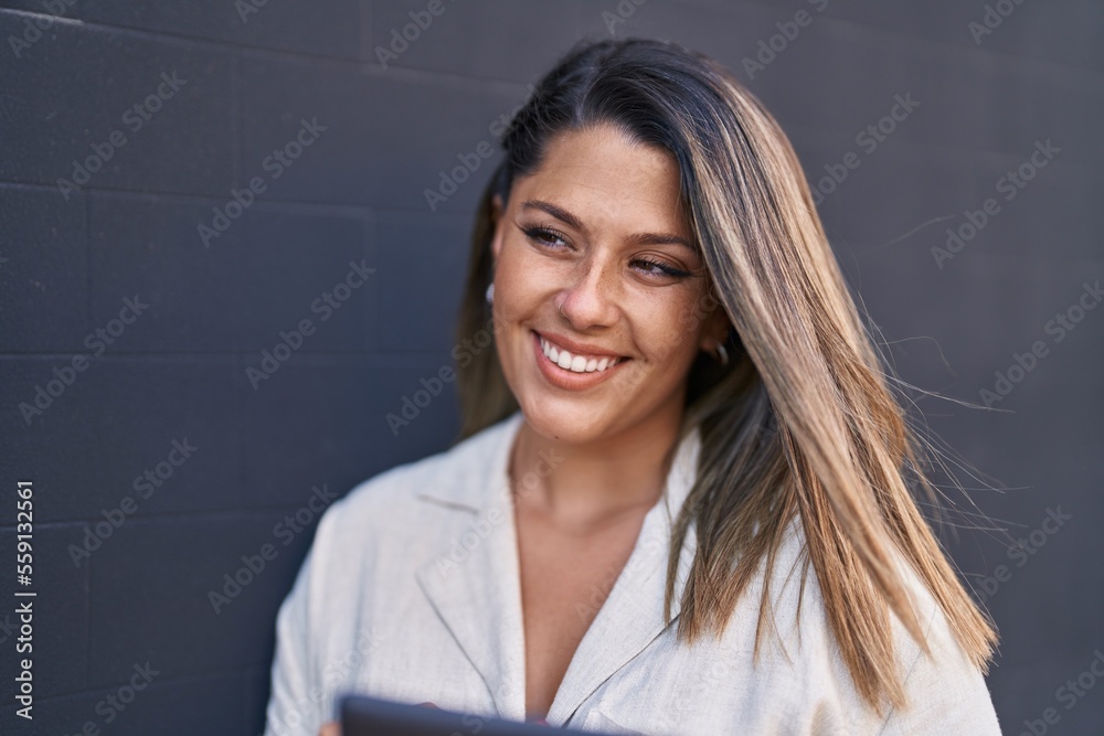 Young hispanic woman smiling confident using touchpad standing by wall Young hispanic woman smiling confident using touchpad standing by wall