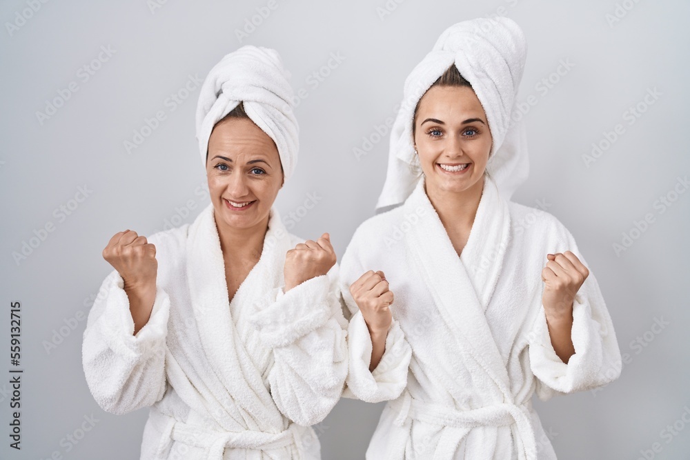 Middle age woman and daughter wearing white bathrobe and towel celebrating surprised and amazed for success with arms raised and open eyes. winner concept. Middle age woman and daughter wearing white bathrobe and towel celebrating surprised and amazed for success with arms raised and open eyes. winner concept.