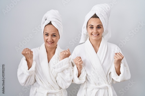 Middle age woman and daughter wearing white bathrobe and towel celebrating surprised and amazed for success with arms raised and open eyes. winner concept.