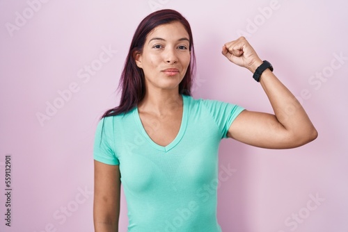 Young hispanic woman standing over pink background strong person showing arm muscle  confident and proud of power