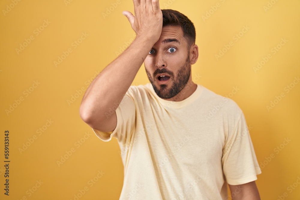 Handsome hispanic man standing over yellow background surprised with hand on head for mistake, remember error. forgot, bad memory concept. Handsome hispanic man standing over yellow background surprised with hand on head for mistake, remember error. forgot, bad memory concept.