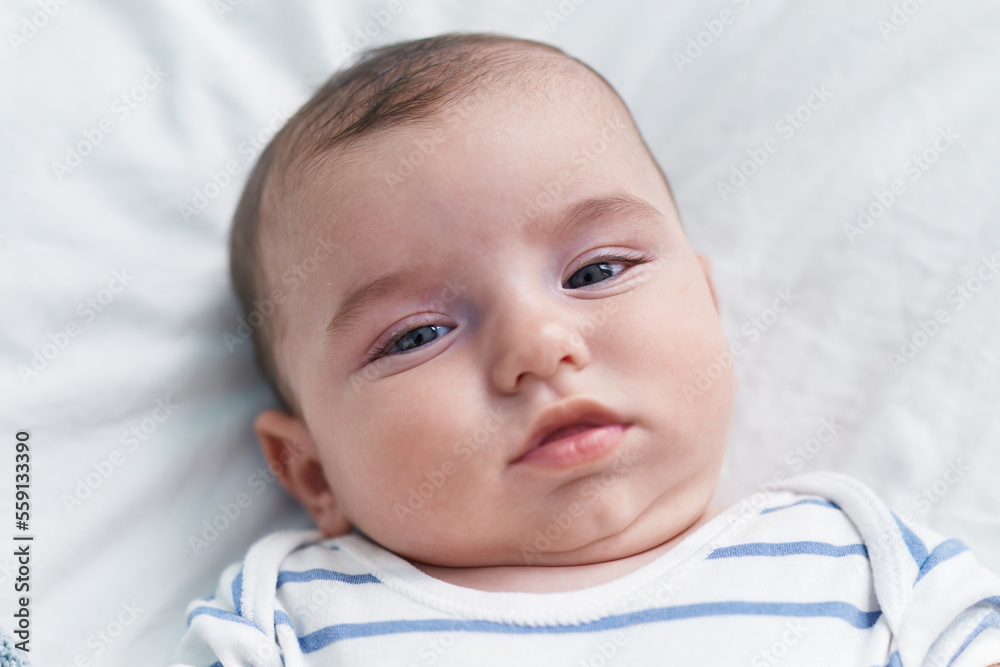 Adorable caucasian baby lying on bed with relaxed expression at bedroom Adorable caucasian baby lying on bed with relaxed expression at bedroom