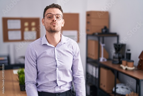 Young hispanic man at the office looking at the camera blowing a kiss on air being lovely and sexy. love expression.