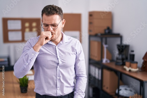 Young hispanic man at the office feeling unwell and coughing as symptom for cold or bronchitis. health care concept.