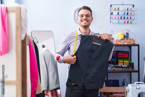 Photography Young hispanic man tailor smiling confident holding waistcoat at tailor shop