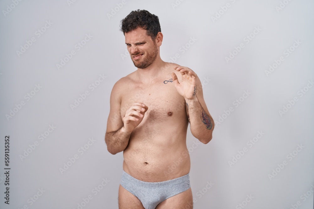 Young hispanic man standing shirtless wearing underware disgusted expression, displeased and fearful doing disgust face because aversion reaction.