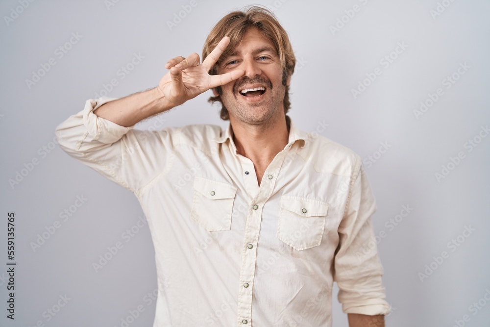 Middle age man standing over isolated background doing peace symbol with fingers over face, smiling cheerful showing victory Middle age man standing over isolated background doing peace symbol with fingers over face, smiling cheerful showing victory