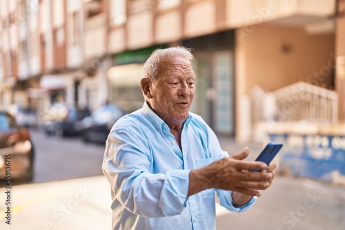 Senior grey-haired man smiling confident using smartphone at street