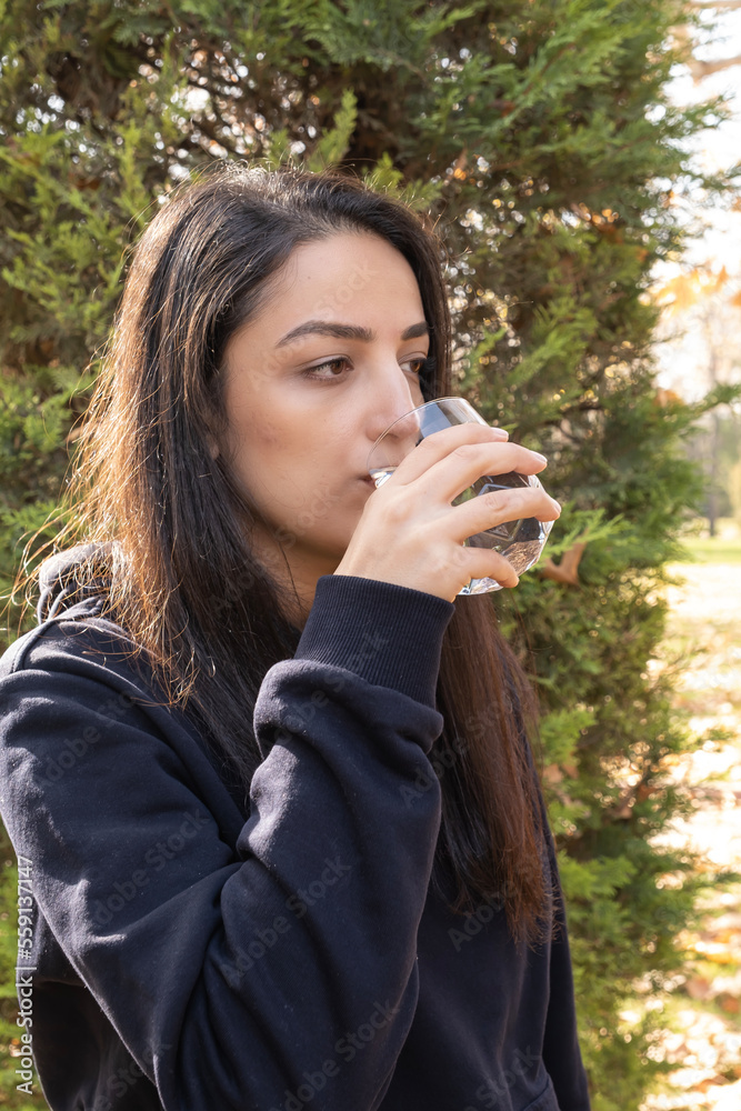 Drinking water, vertical image of caucasian woman drinking water. Healthy habit concept idea. Standing outdoor, autumn season, nature background. Copy space. Drinking water, vertical image of caucasian woman drinking water. Healthy habit concept idea. Standing outdoor, autumn season, nature background. Copy space.
