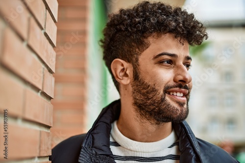 Young arab man smiling leaning on bricks wall