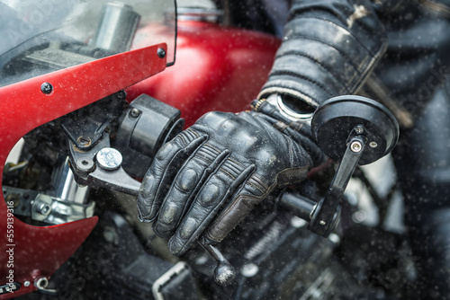 Hand in safety glove on red motorcycle handlebar during snowfall