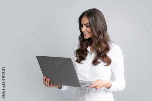 Cheerful business woman standing over grey wall with laptop computer. Portrait of pretty, charming, stylish, clever woman with open laptop chatting, using internet, isolated on grey background.