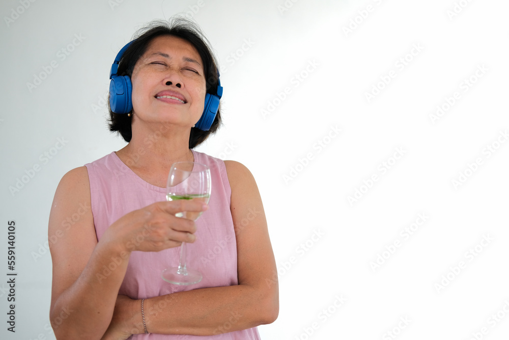 Woman standing with a glass in her hand, listening to music from blue headphone Woman standing with a glass in her hand, listening to music from blue headphone