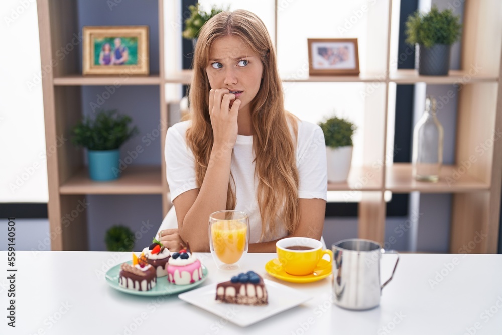Young caucasian woman eating pastries t for breakfast looking stressed and nervous with hands on mouth biting nails. anxiety problem.