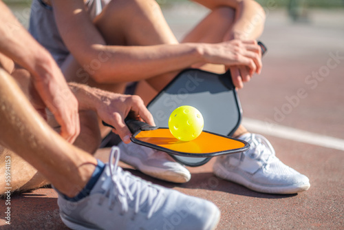  pickleball game, relaxing pickleball players couple with yellow ball with paddle sitting after game, outdoor sport leisure activity. photo