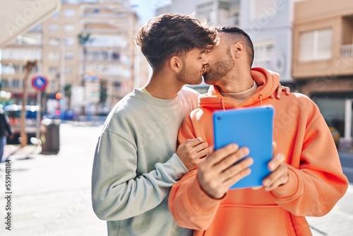 Two man couple using touchpad and kissing at street
