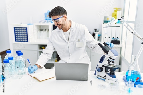 Handsome hispanic man working as scientific with microscope and laptop at laboratory