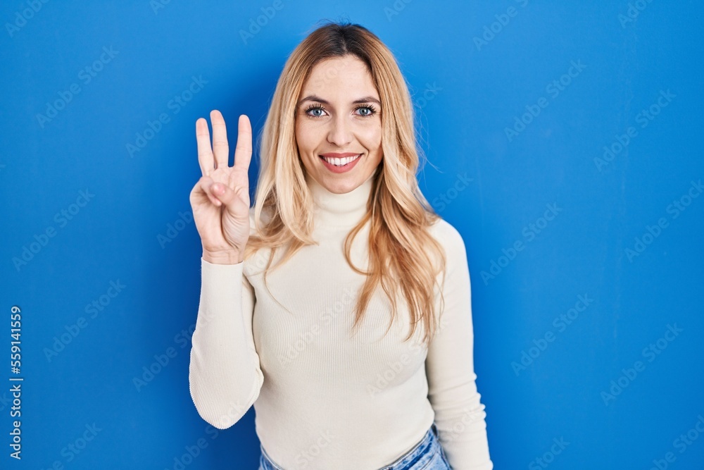 Young caucasian woman standing over blue background showing and pointing up with fingers number three while smiling confident and happy. Young caucasian woman standing over blue background showing and pointing up with fingers number three while smiling confident and happy.