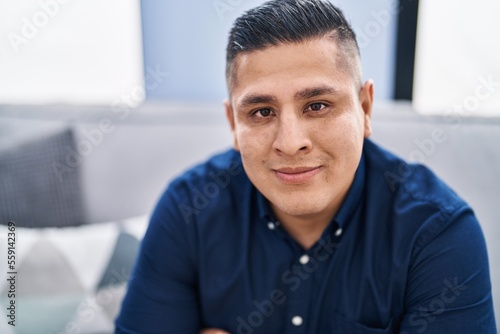 Young latin man smiling confident sitting on sofa at home