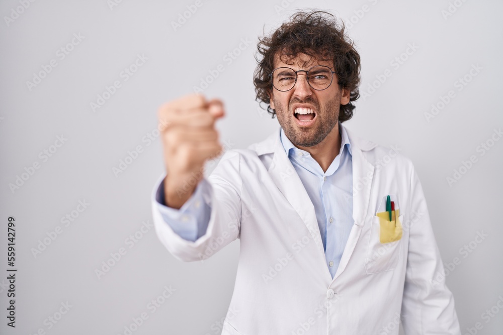 Hispanic young man wearing doctor uniform angry and mad raising fist frustrated and furious while shouting with anger. rage and aggressive concept.