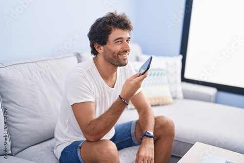 Young hispanic man talking on the smartphone sitting on sofa at home © Krakenimages.com