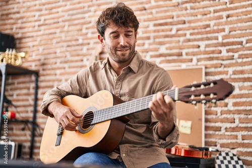 Young man musician smiling confident playing classical guitar at music studio photo