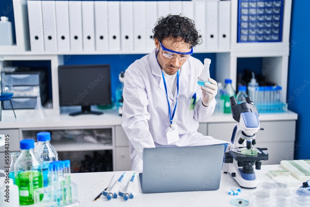 Young hispanic man scientist using laptop holding test tube at laboratory Young hispanic man scientist using laptop holding test tube at laboratory