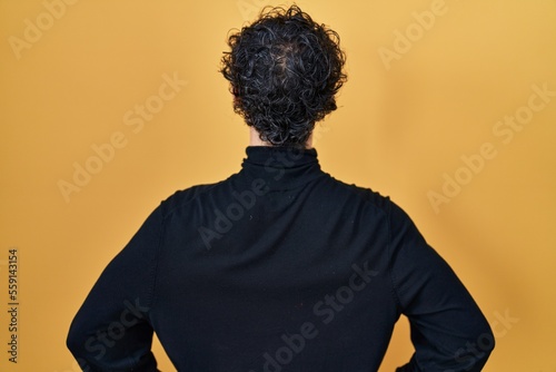 Hispanic man standing over yellow background standing backwards looking away with arms on body