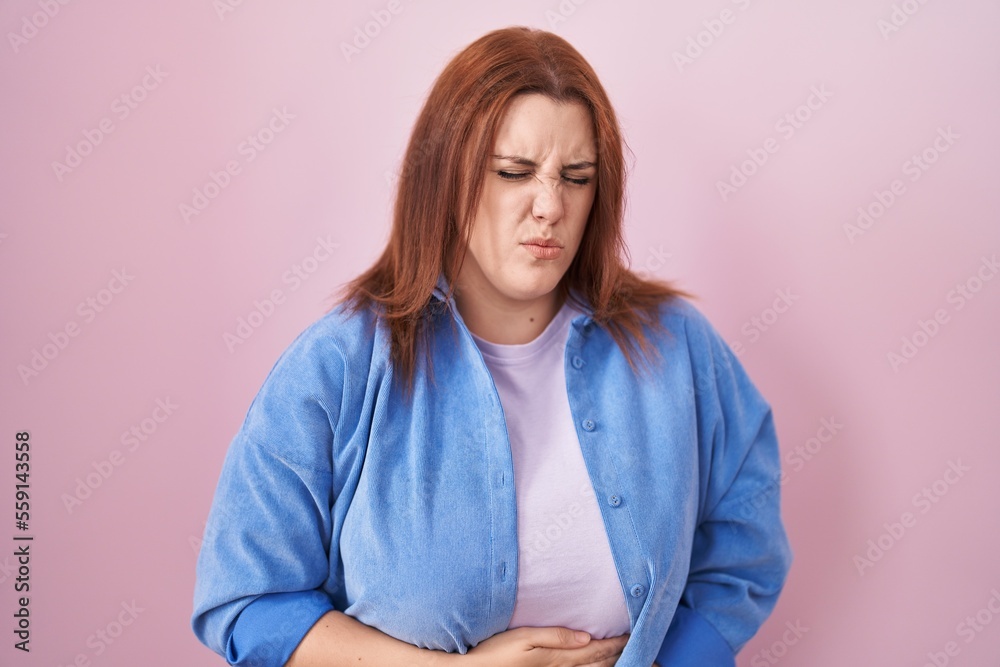 Young hispanic woman with red hair standing over pink background with hand on stomach because indigestion, painful illness feeling unwell. ache concept. Young hispanic woman with red hair standing over pink background with hand on stomach because indigestion, painful illness feeling unwell. ache concept.