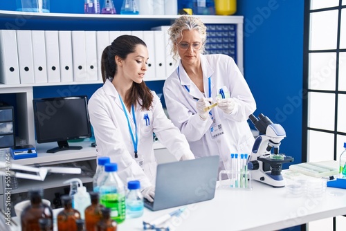 Two women scientists using laptop writing on urine test tube at laboratory