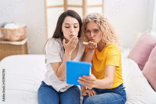 Two women mother and daughter having video call sitting on bed at bedroom