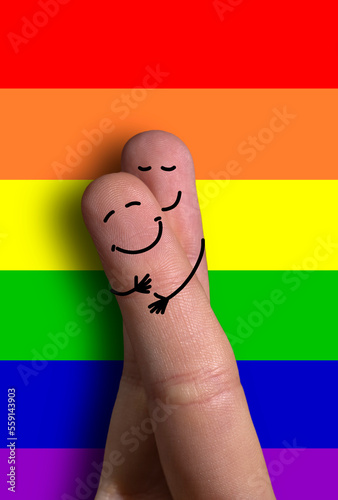 deux personnages entrelacés sont dessinés sur des doigts. En arrière plan, on voit le drapeau arc en ciel LGBT