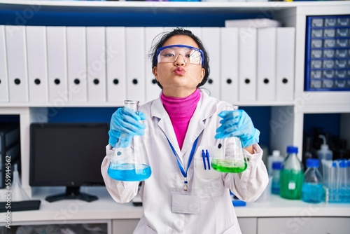 Young asian woman working at scientist laboratory looking at the camera blowing a kiss being lovely and sexy. love expression.