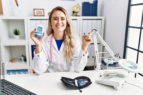 Young beautiful doctor woman holding glucose meter smiling happy pointing with hand and finger to the side