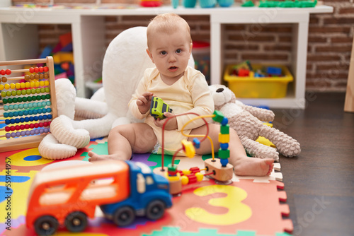 Adorable caucasian baby holding hoop toy sitting on floor at kindergarten