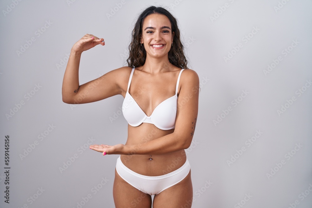 Young hispanic woman wearing white lingerie gesturing with hands showing big and large size sign, measure symbol. smiling looking at the camera. measuring concept. Young hispanic woman wearing white lingerie gesturing with hands showing big and large size sign, measure symbol. smiling looking at the camera. measuring concept.