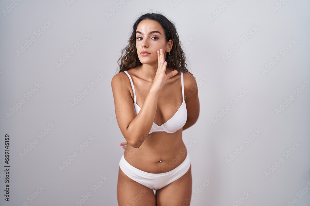 Fototapeta premium Young hispanic woman wearing white lingerie hand on mouth telling secret rumor, whispering malicious talk conversation