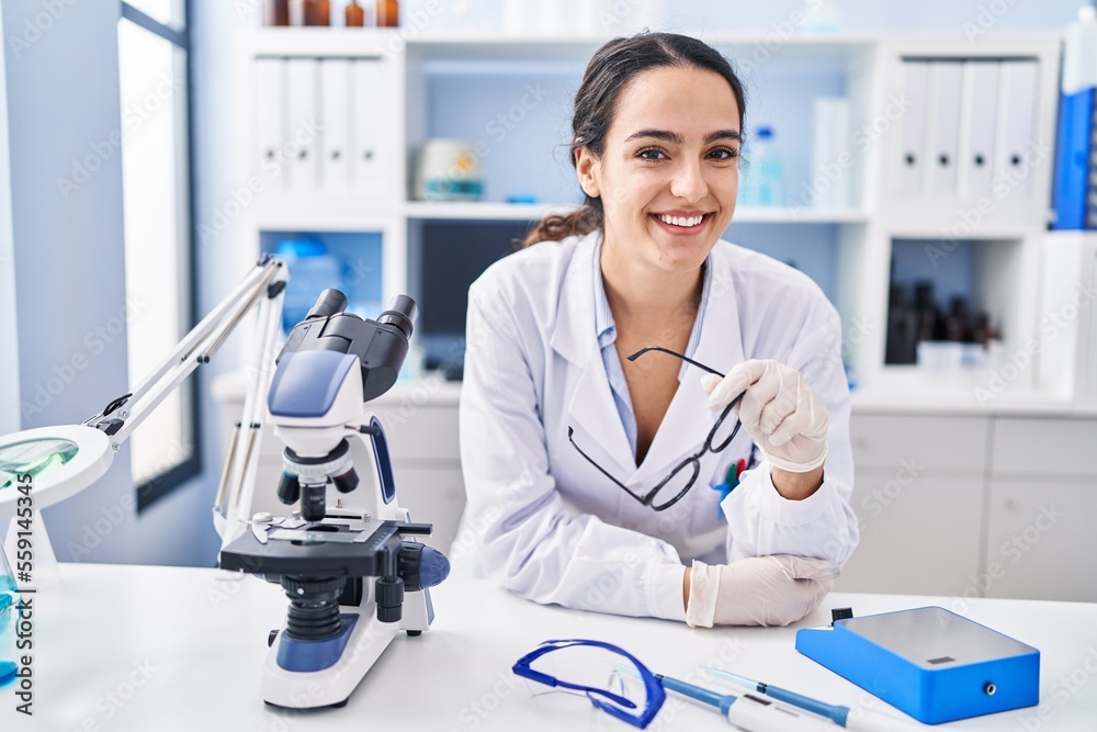 Young hispanic woman wearing scientist uniform smiling confident at laboratory