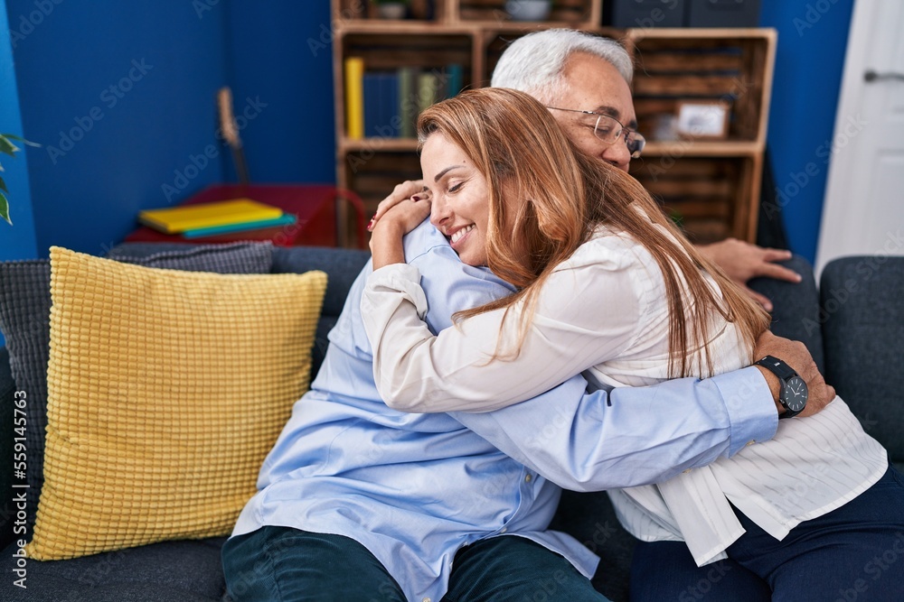 Obraz premium Middle age man and woman couple hugging each other sitting on sofa at home