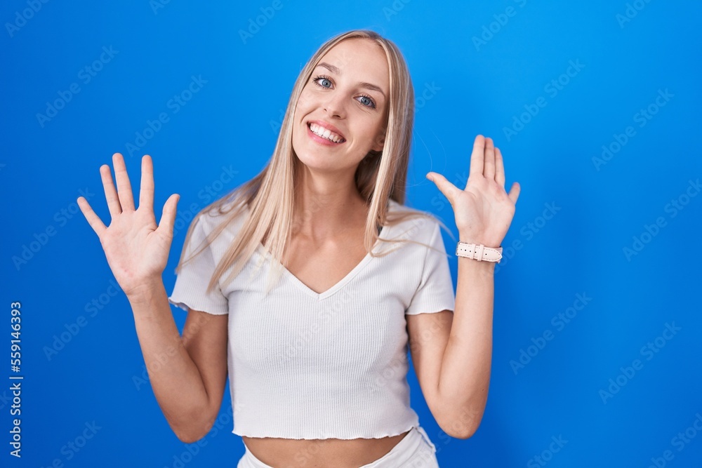 Fototapeta premium Young caucasian woman standing over blue background showing and pointing up with fingers number ten while smiling confident and happy.