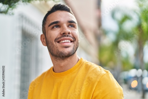 Tableau sur toile Young hispanic man smiling confident looking to the sky at street