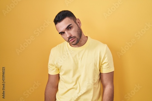 Young hispanic man standing over yellow background looking sleepy and tired, exhausted for fatigue and hangover, lazy eyes in the morning.