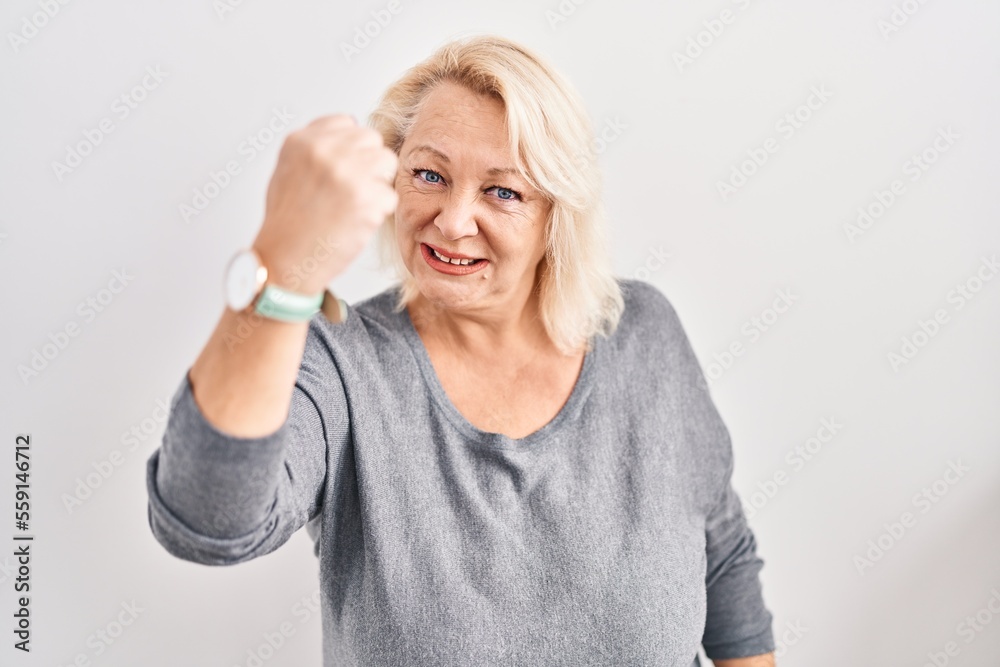 Middle age caucasian woman standing over white background angry and mad raising fist frustrated and furious while shouting with anger. rage and aggressive concept. Middle age caucasian woman standing over white background angry and mad raising fist frustrated and furious while shouting with anger. rage and aggressive concept.