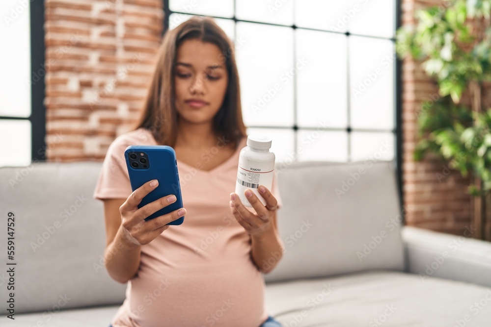 Young latin woman pregnant using smartphone holding bottle of pills at home Young latin woman pregnant using smartphone holding bottle of pills at home