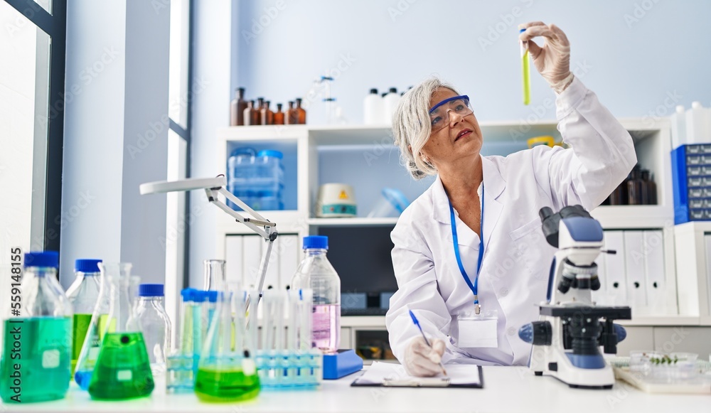 Fototapeta premium Middle age woman wearing scientist uniform holding test tube at laboratory