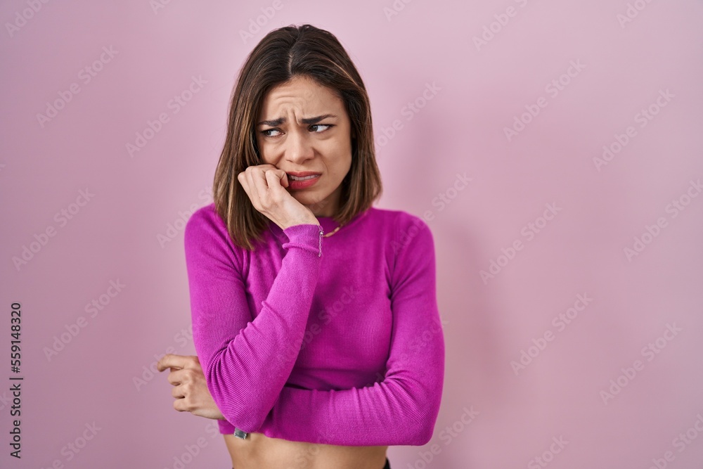 Hispanic woman standing over pink background looking stressed and nervous with hands on mouth biting nails. anxiety problem. Hispanic woman standing over pink background looking stressed and nervous with hands on mouth biting nails. anxiety problem.