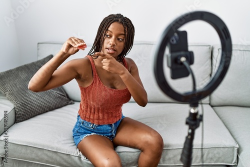 Young african american woman holding menstrual cup recording video tutorial at home