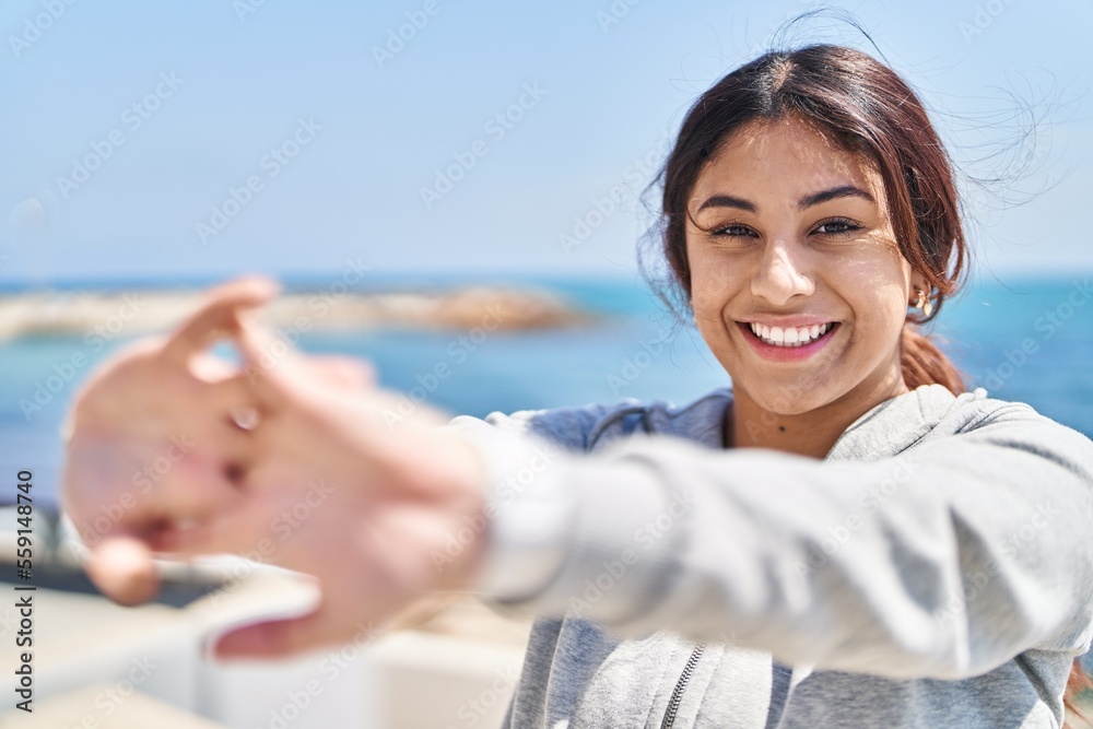 Young hispanic woman stretching arms training at seaside