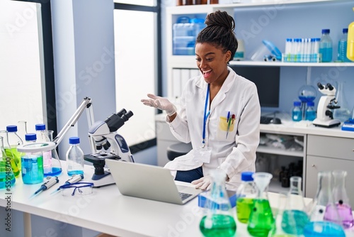 Young african american with braids working at scientist laboratory with laptop celebrating achievement with happy smile and winner expression with raised hand