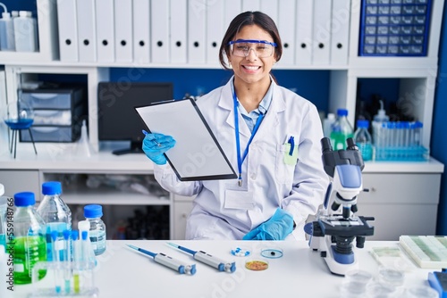 Hispanic young woman working at scientist laboratory winking looking at the camera with sexy expression  cheerful and happy face.